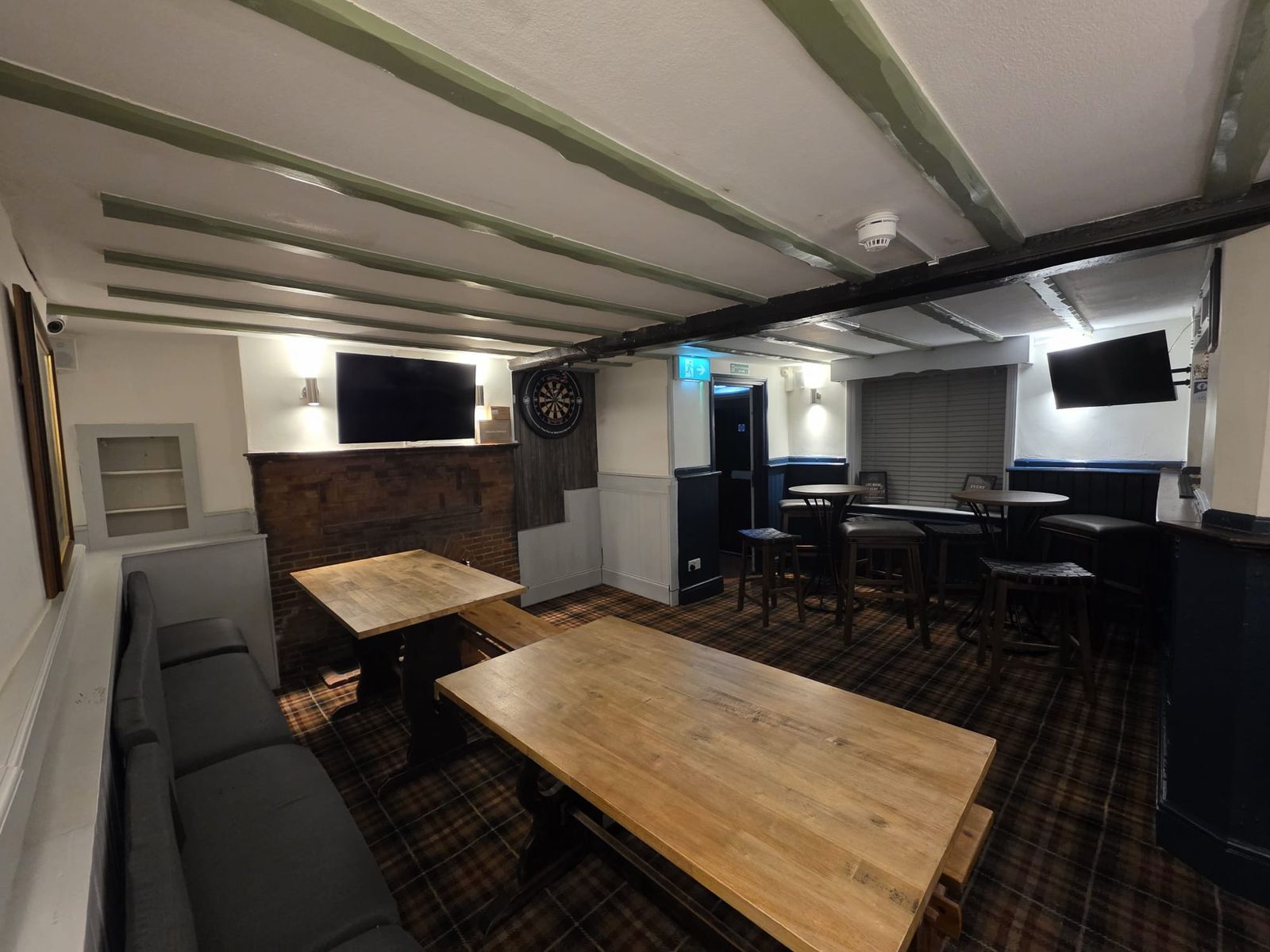 The back room with a dartboard, TVs, bench seating and tartan carpet